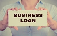 Business woman hands holding white card sign with business loan text message isolated on grey wall office background. Retro instagram style image-1
